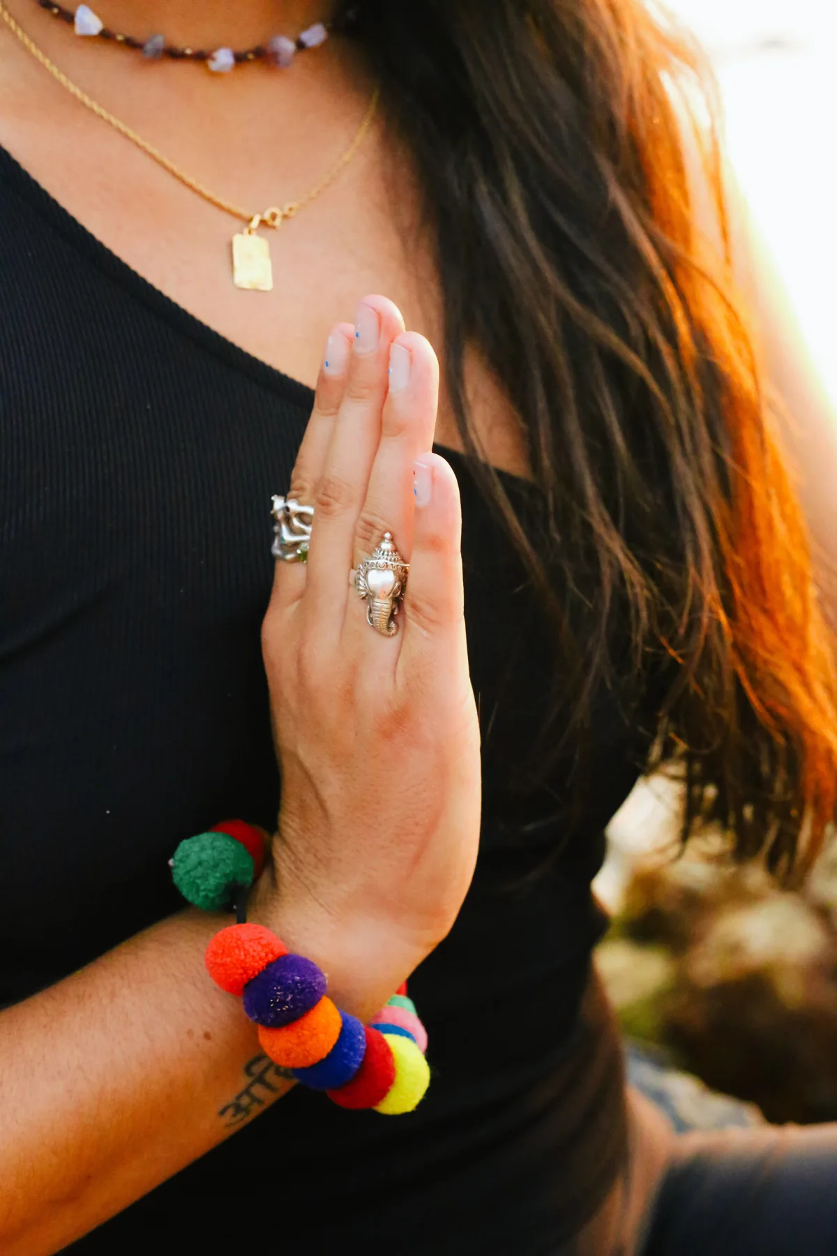 Détail des mains de Lauriane jointes, ornées de bagues et d’un bracelet coloré
